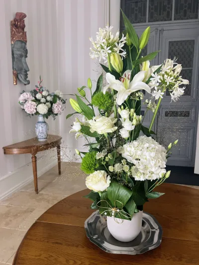 Grande composition blanche de lys, agapanthes et hortensias dans un vase blanc, au centre d'une table ronde