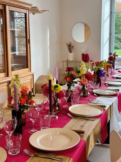 Longue table de réception dressée en rose fuchsia, avec des petits vases de fleurs colorées et des bougies