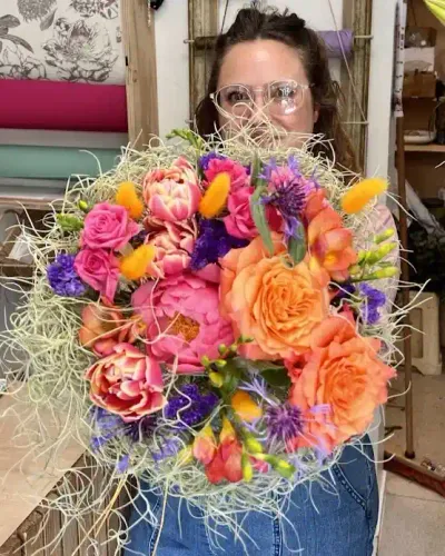 Léa Mahé tient devant elle un bouquet de roses orange, tulipes, pivoine corail et queues de lièvre jaunes
