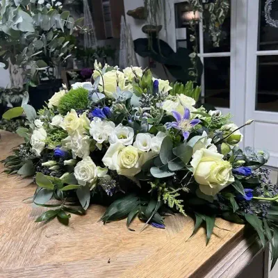 Grande raquette de deuil de roses blanches, lisianthus, clématites et fleurs bleues, posée sur une table en boutique