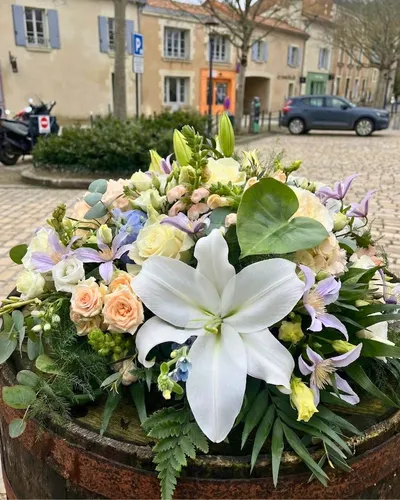 Composition de condoléances autour d'un lys blanc, roses pêche, clématites mauves et anthurium vert, sur un tonneau