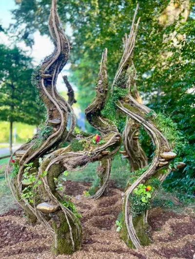 Scénographie végétale en spirales de lianes et de mousse dressée dans un parc, avec champignons et fleurs