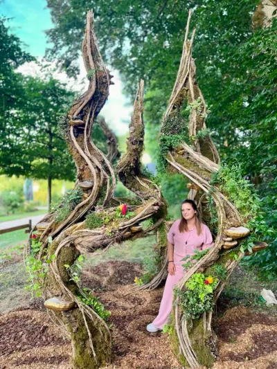 Léa Mahé pose au pied de sa scénographie végétale en spirales de lianes et de mousse, installée dans un parc