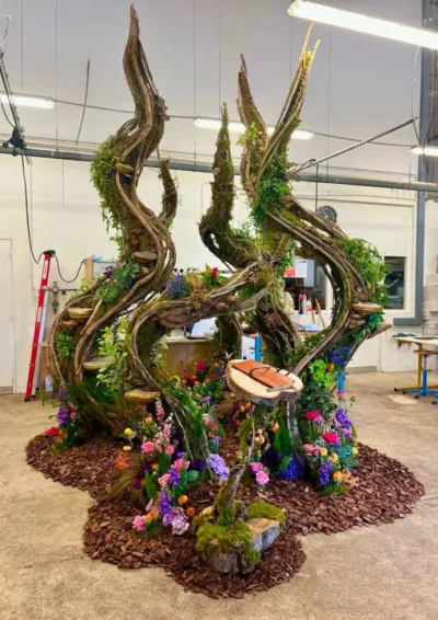 Scénographie végétale en spirales de lianes assemblée en atelier, base de paillis couverte de fleurs colorées