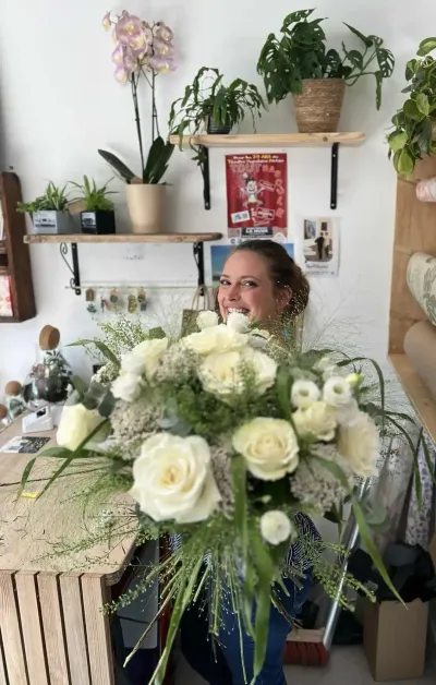 Léa Mahé souriante derrière un grand bouquet de roses blanches et de graminées, dans la boutique Herborium