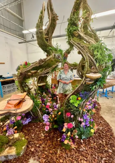 Léa Mahé au milieu de sa scénographie végétale terminée en atelier, spirales de lianes et tapis de fleurs