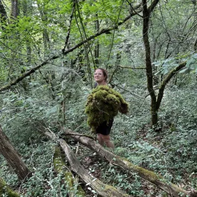Léa Mahé récolte de la mousse fraîche en forêt, les bras chargés, pour habiller sa scénographie végétale