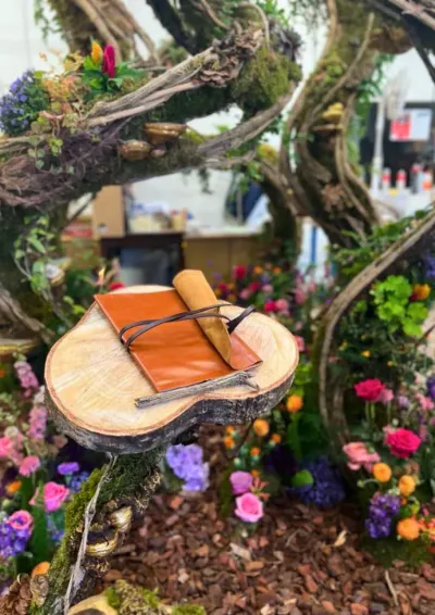 Livre d'or en cuir posé sur une rondelle de bois au cœur de la scénographie végétale, entouré de fleurs