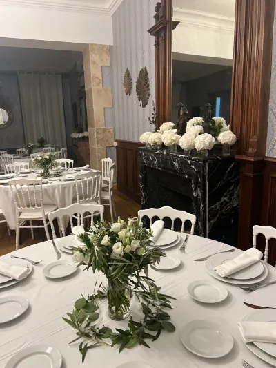Centre de table de réception : lisianthus blancs et branches d'olivier en vase, hortensias blancs sur une cheminée en marbre