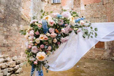 Angle d'arche de mariage en roses pêche, dahlias roses et delphiniums bleus, voile blanc, dans des ruines en pierre