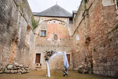Arche de mariage fleurie d'un angle de roses pastel et de delphiniums, voile blanc, au centre d'une cour en ruines