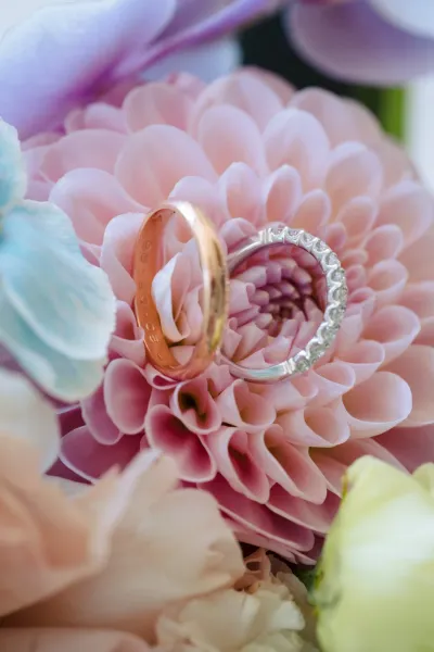 Alliances posées au cœur d'un dahlia rose pâle, entre les fleurs bleues et pêche d'un bouquet de mariée