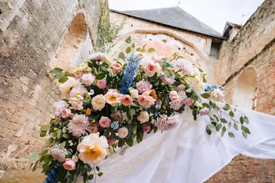 Gros plan d'un angle d'arche de mariage : roses pêche et blanches, dahlias roses, delphiniums bleus et feuillage