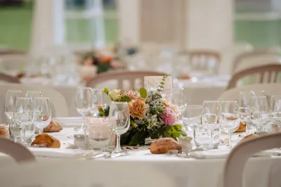 Centre de table de mariage en fleurs pastel sur une nappe blanche, entre verres à pied et petits pains, sous une tente