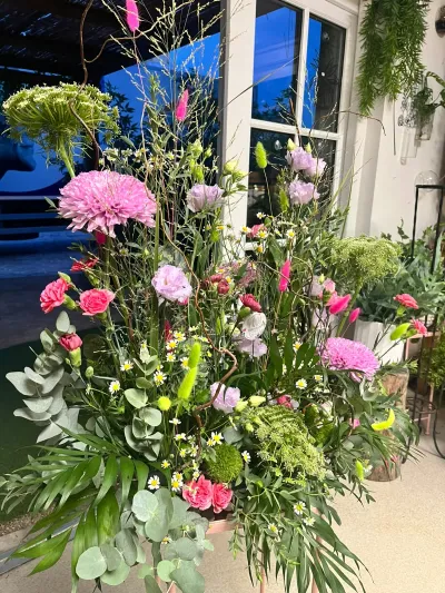 Devant de cercueil haut de dahlias roses, œillets et feuillages variés, devant une porte vitrée
