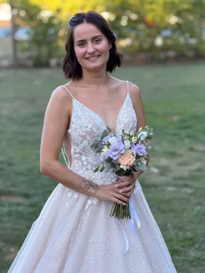 Mariée souriante tenant son bouquet de roses pêche, fleurs lilas et eucalyptus, en robe de dentelle