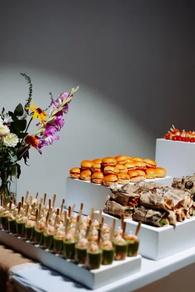 Buffet de mariage : verrines et mini-burgers sur des présentoirs blancs, à côté d'un bouquet de fleurs colorées