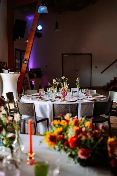 Salle de réception de mariage aux tables rondes fleuries de dahlias orange, de tournesols et de soliflores