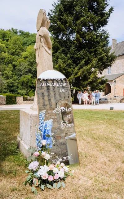 Panneau de bienvenue d'un mariage, fleuri à son pied de delphiniums bleus, roses et fleurs blanches, dans un parc