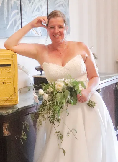 Mariée souriante tenant un bouquet de mariée retombant de roses blanches, jasmin et feuillages, robe bustier en dentelle