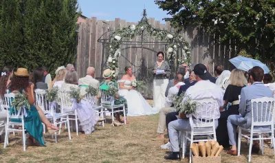 Cérémonie de mariage en plein air sous une gloriette fleurie de roses blanches et de feuillages, chaises ornées d'olivier