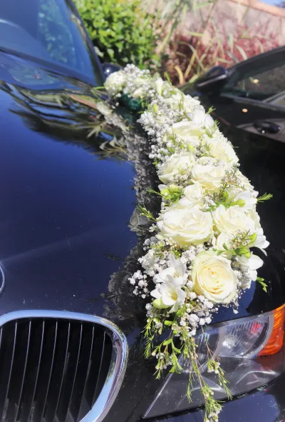 Composition florale de mariage sur le capot d'une voiture noire, roses blanches, gypsophile, freesias et fleurs de cire
