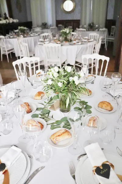 Centre de table de mariage, lisianthus blancs et olivier en vase, branches d'eucalyptus en chemin de table sur nappe blanche