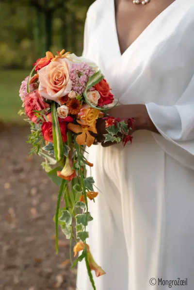 Mariée en robe blanche tenant un bouquet de mariée en cascade, roses pêche et orange, lierre retombant