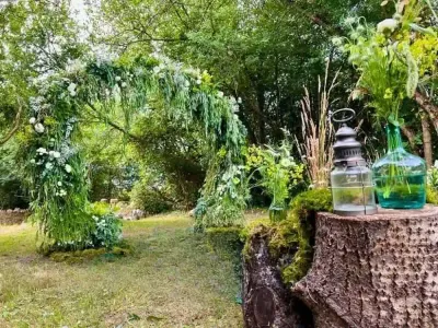 Arche végétale de mariage en saule et fleurs blanches dans un jardin, lanterne et vase vert sur une souche