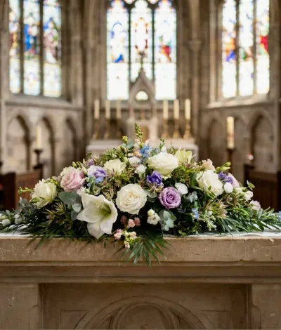 Raquette de deuil de roses blanches et mauves, lys et petites fleurs bleues, posée sur l'autel d'une église