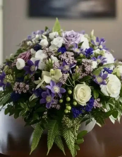 Coussin de fleurs de deuil rond aux tons violet et blanc, création artisanale pour cérémonie funéraire.