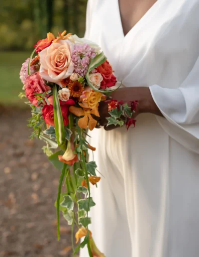 Mariée en robe blanche tenant un élégant bouquet retombant aux couleurs chaudes, fleuriste mariage 86