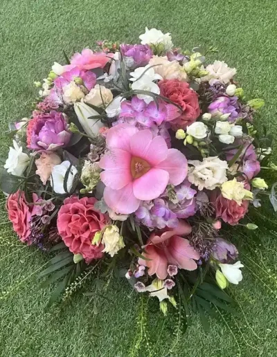 Composition florale de deuil circulaire et genereuse avec une dominante de fleurs roses mauves et blanches