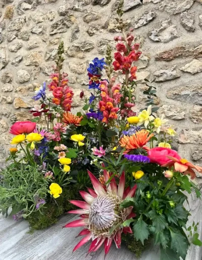Composition florale originale style jardin avec Protea mufliers et fleurs champetres devant un mur en pierres