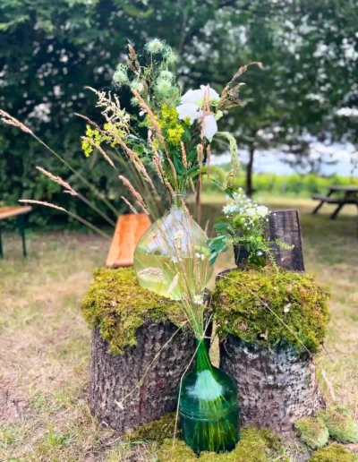 Décoration de mariage champetre rustique tronc arbre mousse dame jeanne fleurs sauvages nigelle herbes folles bancs bois arriere plan