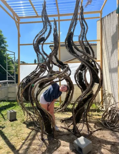 Lea Mahe regarde a travers les courbes de sa scenographie vegetale en cours de construction