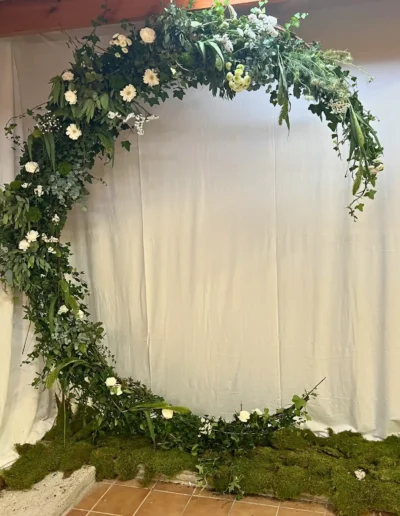 arche mariage circulaire photobooth dense feuillage vert fleurs blanches base mousse fond uni